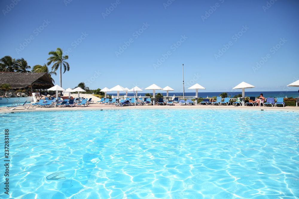 swimming pool with blue water and white umbrellas at a tropical resort. Summer concept background - Sea or Ocean Beach