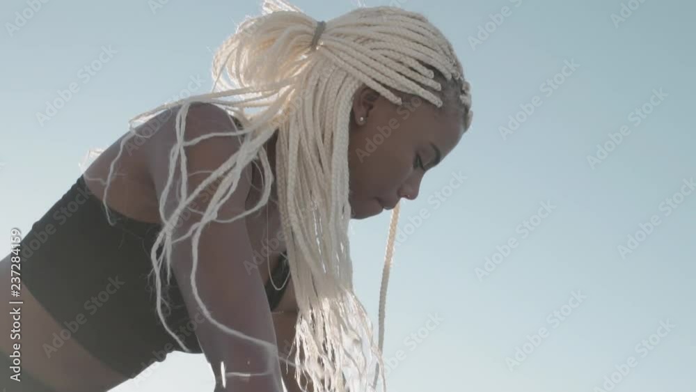 Close up of an african female runner with blond braided hairstyle ready on her marks on a running track. Sprinter looking focused ready to race on the track.