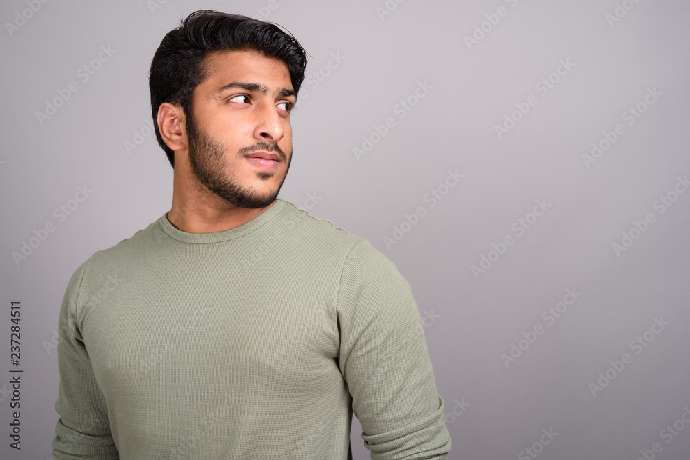 Portrait of young handsome Indian man thinking against gray background Portrait of young handsome Indian man thinking against gray background