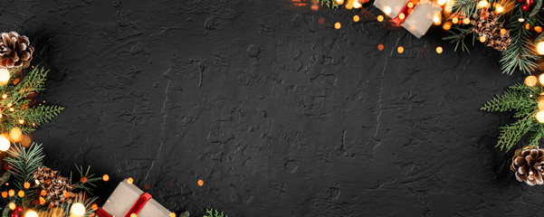 Creative layout frame made of Christmas fir branches, pine cones, gifts on dark background with light. Xmas and New Year theme, bokeh, sparking, glowing. Flat lay, top view, wide composition