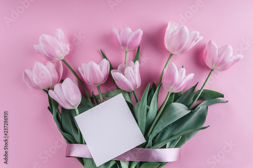 Fototapeta Naklejka Na Ścianę i Meble -  Bouquet of white tulips flowers and sheet of paper over light pink background. Greeting card or wedding invitation. Flat lay, top view, copy space