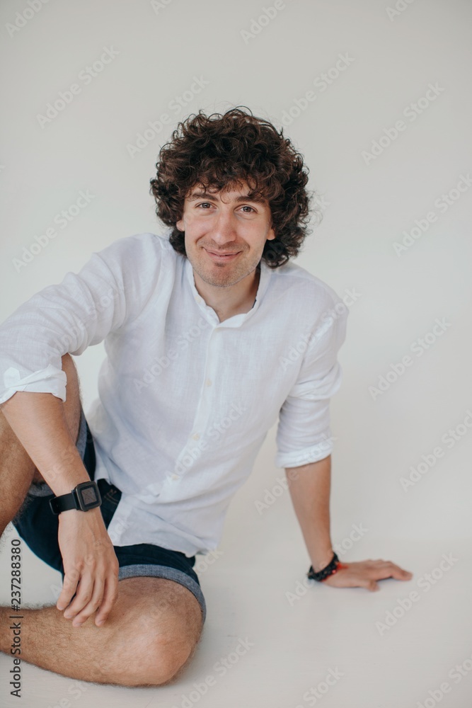 Young smiling curly man sitting on the floor and looking at camera Young smiling curly man sitting on the floor and looking at camera