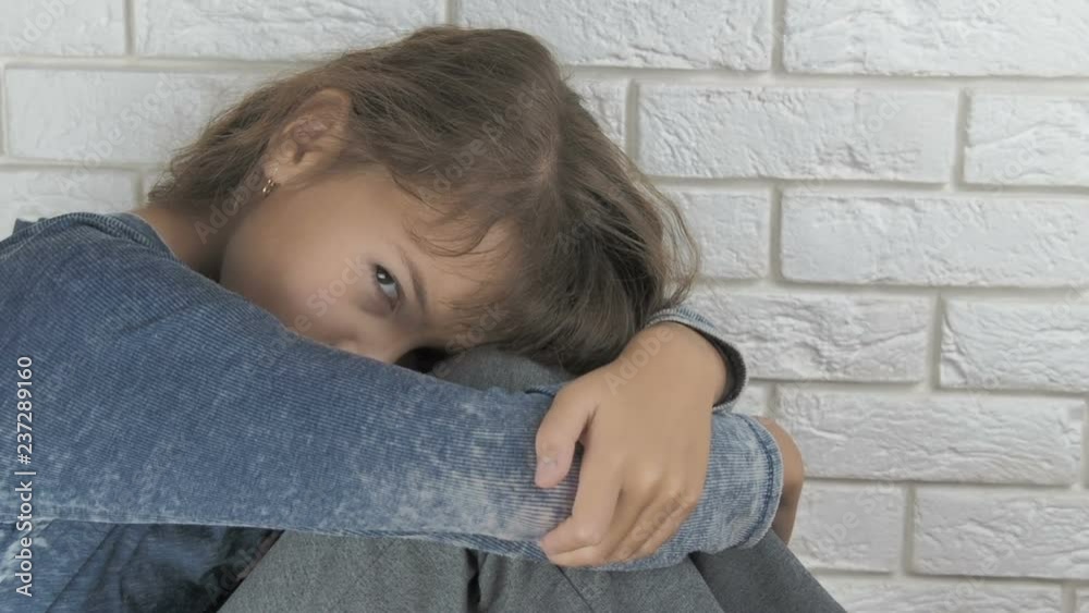 Depressed child. Domestic violence. A sad little girl sits with her knees covering her face. Depressed child. Domestic violence. A sad little girl sits with her knees covering her face.