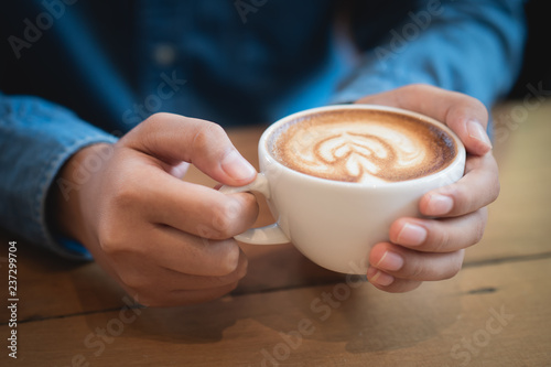 Man hands holding a cup of coffee on wooden table