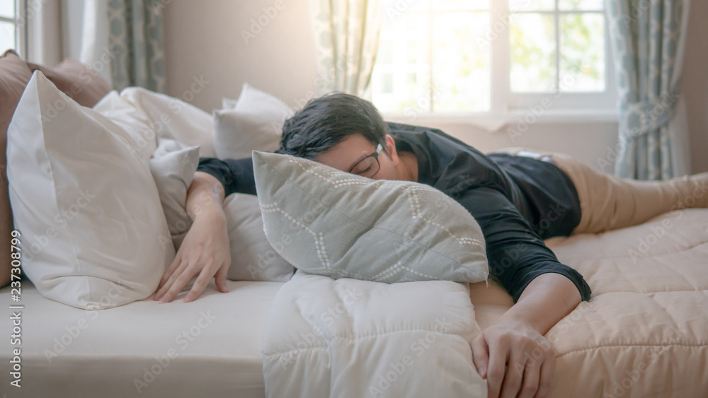 Young Asian man with eyeglasses sleeping on bed in bedroom in the morning. Home living lifestyle concept