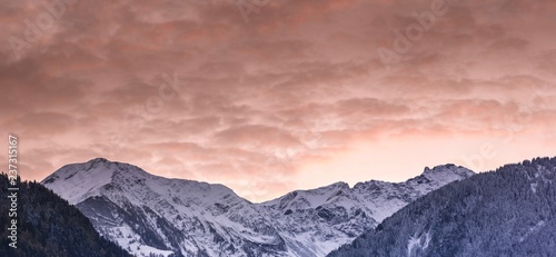 panorama winter mountain landscape with forests in fall colors and snow-capped mountain peaks and valleys under an expressive sunset sky in the Swiss Alps above Bad Ragaz