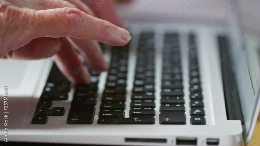 Close up of old person’s palm typing on black laptop keyboard