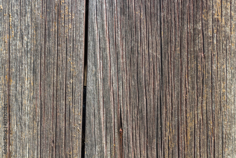 Vertical wood siding from an old barn. The siding is brown and heavily textured. There are two planks separated by a crack.