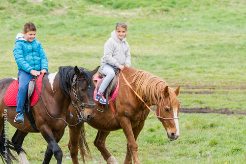 Boy and girl riding horses on the green meadow