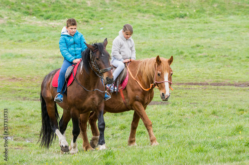 Boy and girl riding horses on the green meadow