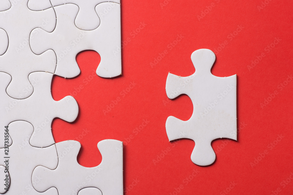 © azrisuratmin - Unfinished white jigsaw puzzle pieces on red background