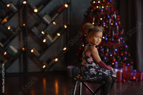 Preschool cheerful little happy girl have a good time at home near bright christmas tree with lights.