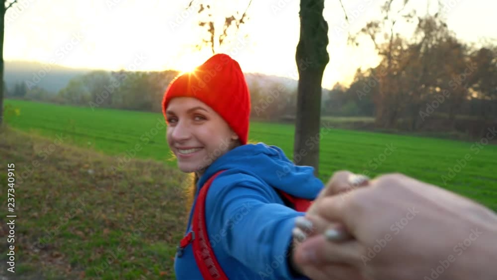 Follow me - happy young woman in red hat pulling guy's hand. Hand in hand walking among the fields in the countryside
