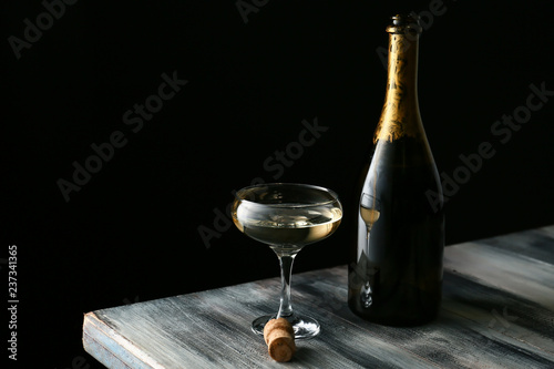 Fotografi Glass and bottle of champagne on wooden table against dark background