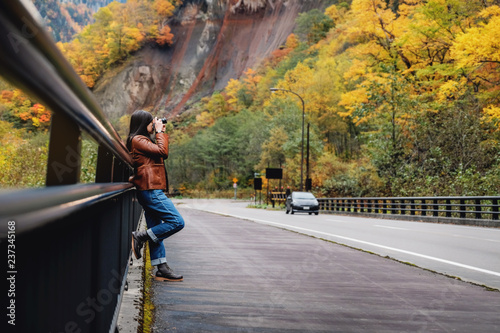 Travel Concept. Young Traveling Woman with Camera taking Photo in Fall and Autumn Nature Scenery