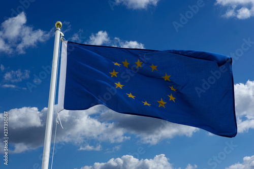 EUROPEAN UNION BLUE FLAG WITH GOLD STARS AND BLUE SKY WITH WHITE CLOUDS