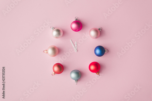 Clock hands with colorful pastel decoration balls on pink painted wall. Minimal time concept. Chrismas eve or new year idea. photo