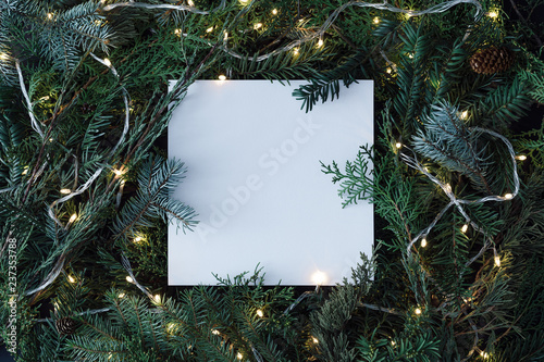 Creative layout made of Christmas tree branches with paper card note and christmas lights. Flat lay. Nature New Year concept.