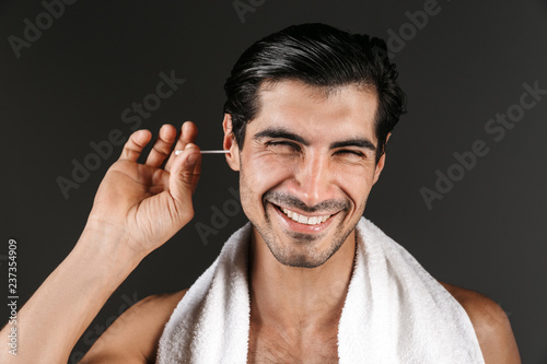 Handsome young man posing isolated over dark wall background cleaning his ears.