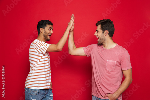 Two cheerful young men standing isolated over red photo