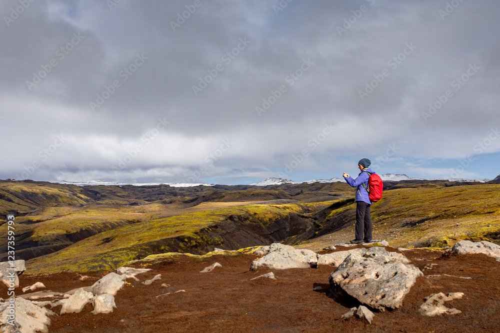 A young woman with a backpack travels around Iceland. Front view of a tourist walking through a mountainous area on a sunny day.