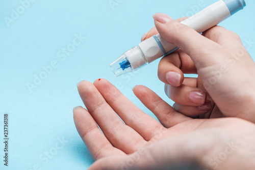 cropped view of female hands making glucose level test with needle on blue background