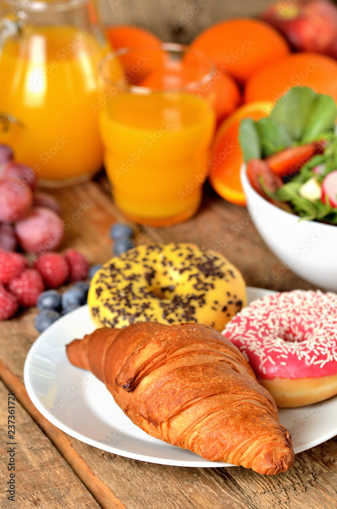 Close-up of croissant and donuts, orange juice and fresh salad - breakfast on wooden table vertical photo
