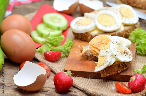 Wholegrain bread with butter, hard-boiled eggs, fresh radishes, tomatoes, salad and cucumbers in background