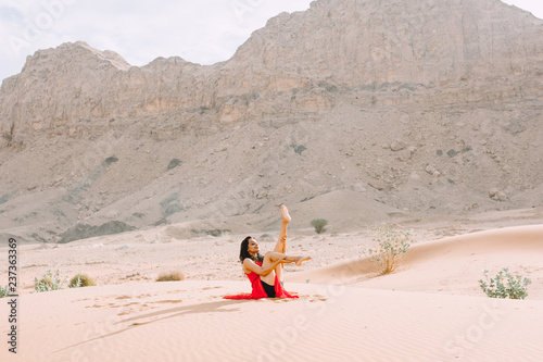 Young beautiful Indian woman doing yoga in the desert in red long dress photo