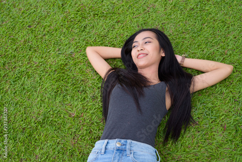 Happy young beautiful Asian woman laying down on grass at the park