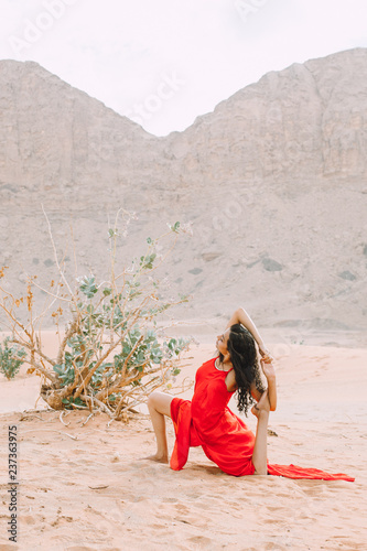 Young beautiful Indian woman doing yoga in the desert in red long dress photo