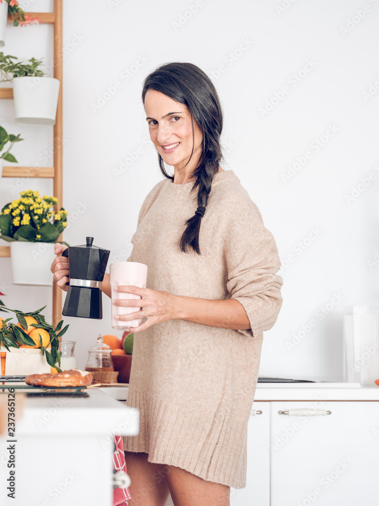 Young woman filling cup from teapot in kitchen Young woman filling cup from teapot in kitchen