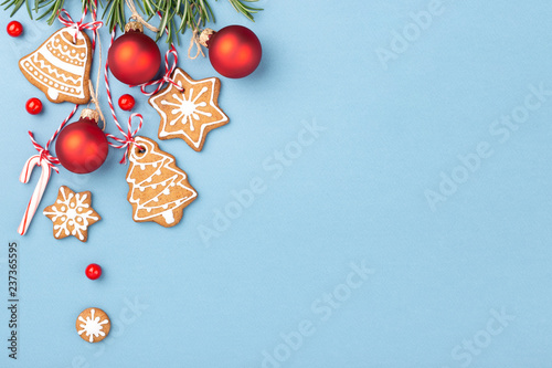 Gingerbread cookies with red Christmas balls and candy cane lollipop hanging over blue background and decorated with berries and rosemary. Top view, copy space. photo