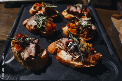 Tasty and nutritious sandwich with meat, fried tomatoes and herbs on a black plate on a wooden table photo