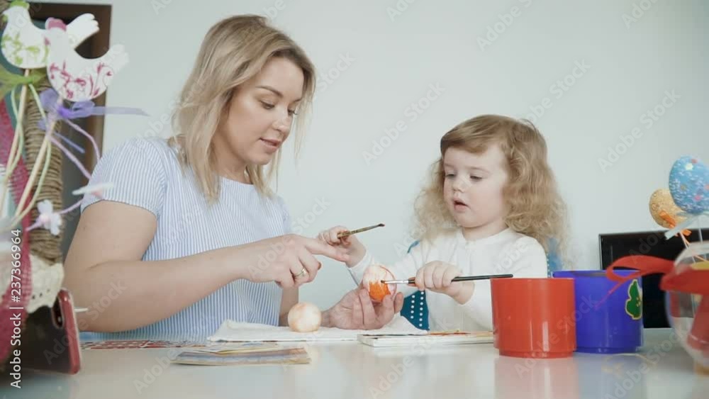 Happy Easter! Mother and her little daughte painting Easter eggs at the festive table with basket and eggs. Slow Motion Happy Easter! Mother and her little daughte painting Easter eggs at the festive table with basket and eggs. Slow Motion