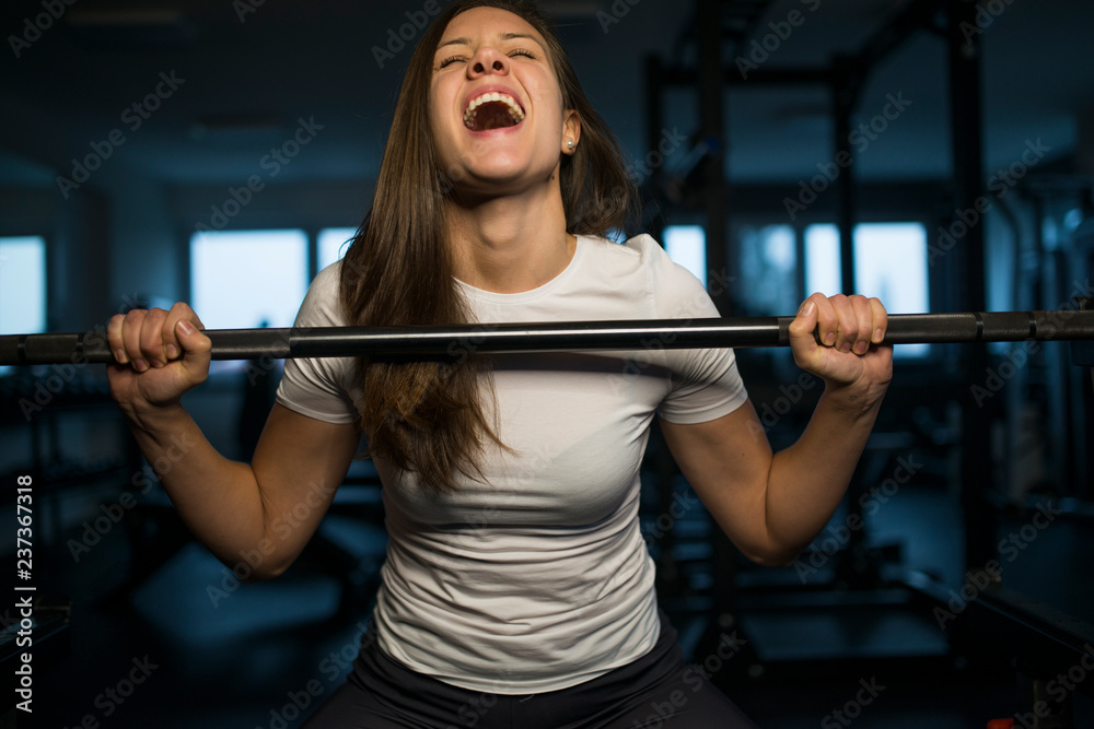 Happy successful young sporty woman in the gym lifting barbell