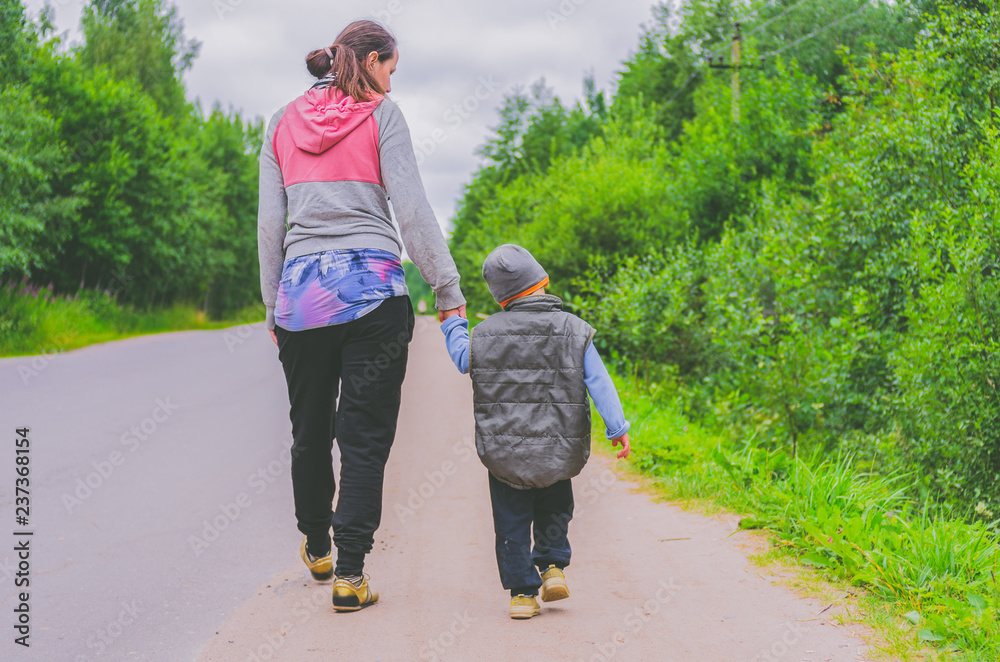 Fototapeta premium Mom and little son are walking along the road in the countryside