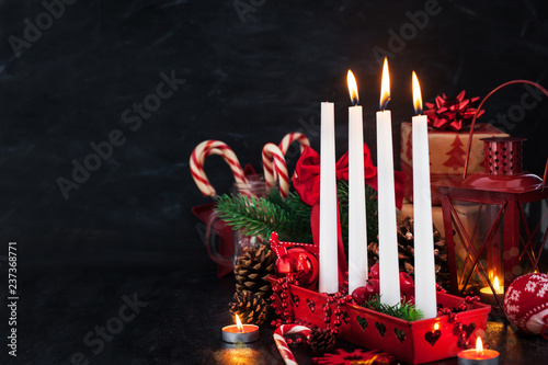 Four Christmas Advent candles and holiday decorations around on dark background