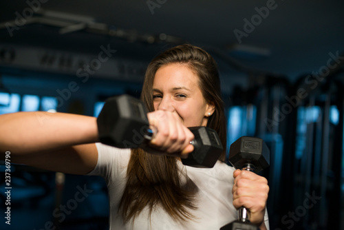 Shy young female during the dumbbell training, fitness background