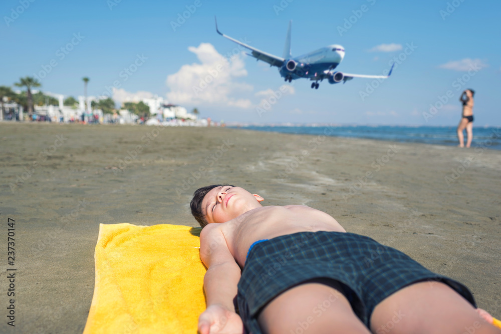 Teen  boy lies on yellow towel and sunbathes on the beach under the landing planes. Traveling on an airplane with children. Concept