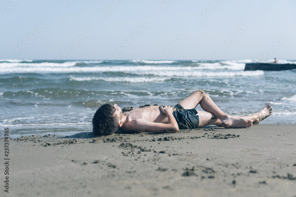 Happy teen boy having fun in the healing mud from the sea on the beach