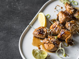 Grilled Asian teriyaki chicken skewers with sesame, leek and citrus juice on a white oval plate on dark grey background