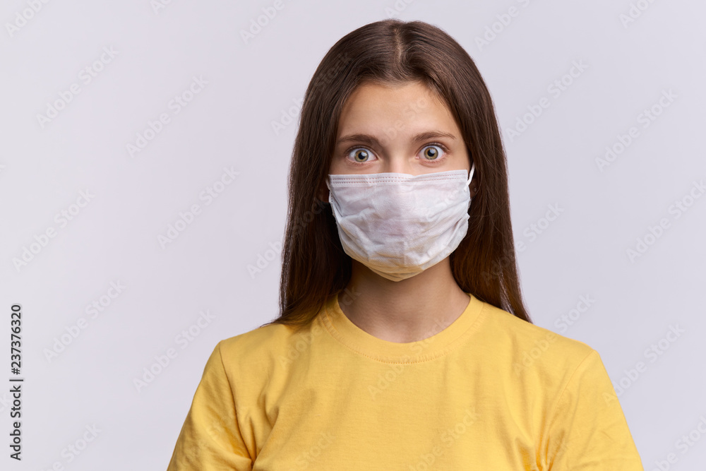 The brunette girl in a protective medical mask opens her eyes wide and looks in front of her. Fear of infection, protection against the spread of the disease The brunette girl in a protective medical mask opens her eyes wide and looks in front of her. Fear of infection, protection against the spread of the disease