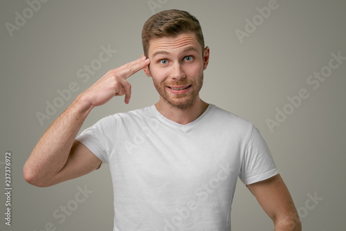 Attractive man holding a finger to his temple and thinks you a fool. The representative of the stronger sex knows the solution to all problems and is confident in his abilities