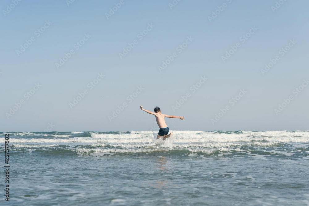 Boy Jumping In Sea Waves with Water Splashes. Concept of summer vacation Boy Jumping In Sea Waves with Water Splashes. Concept of summer vacation