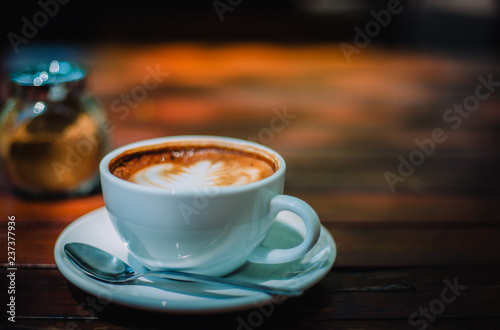 Hot coffee latte cappuccino spiral foam on wooden table in coffee shop cafe with vintage color tone filter background. With copy space for your text.