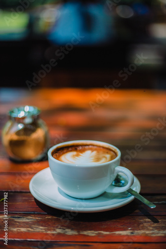 Hot coffee latte cappuccino spiral foam on wooden table in coffee shop cafe with vintage color tone filter background. With copy space for your text.