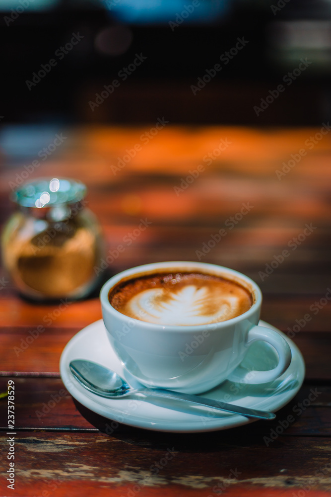 Hot coffee latte cappuccino spiral foam on wooden table in coffee shop cafe with vintage color tone filter background. With copy space for your text. Color tone effect Hot coffee latte cappuccino spiral foam on wooden table in coffee shop cafe with vintage color tone filter background. With copy space for your text. Color tone effect