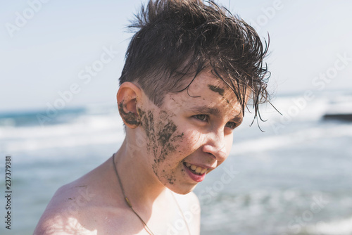Face of happy teen boy in the healing mud from the sea on the beach