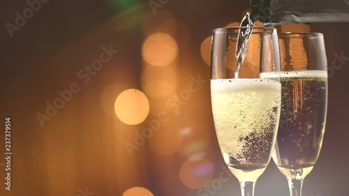 Champagne pouring from a bottle. Two flutes with sparkling wine over golden holiday bokeh blinking background. Celebration. Slow motion 4K UHD video footage. 3840X2160 photo
